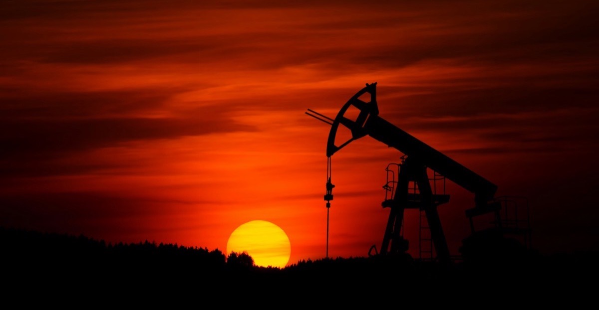 A pumpjack silhouetted against a deep red sunset as the sun touches the horizon.